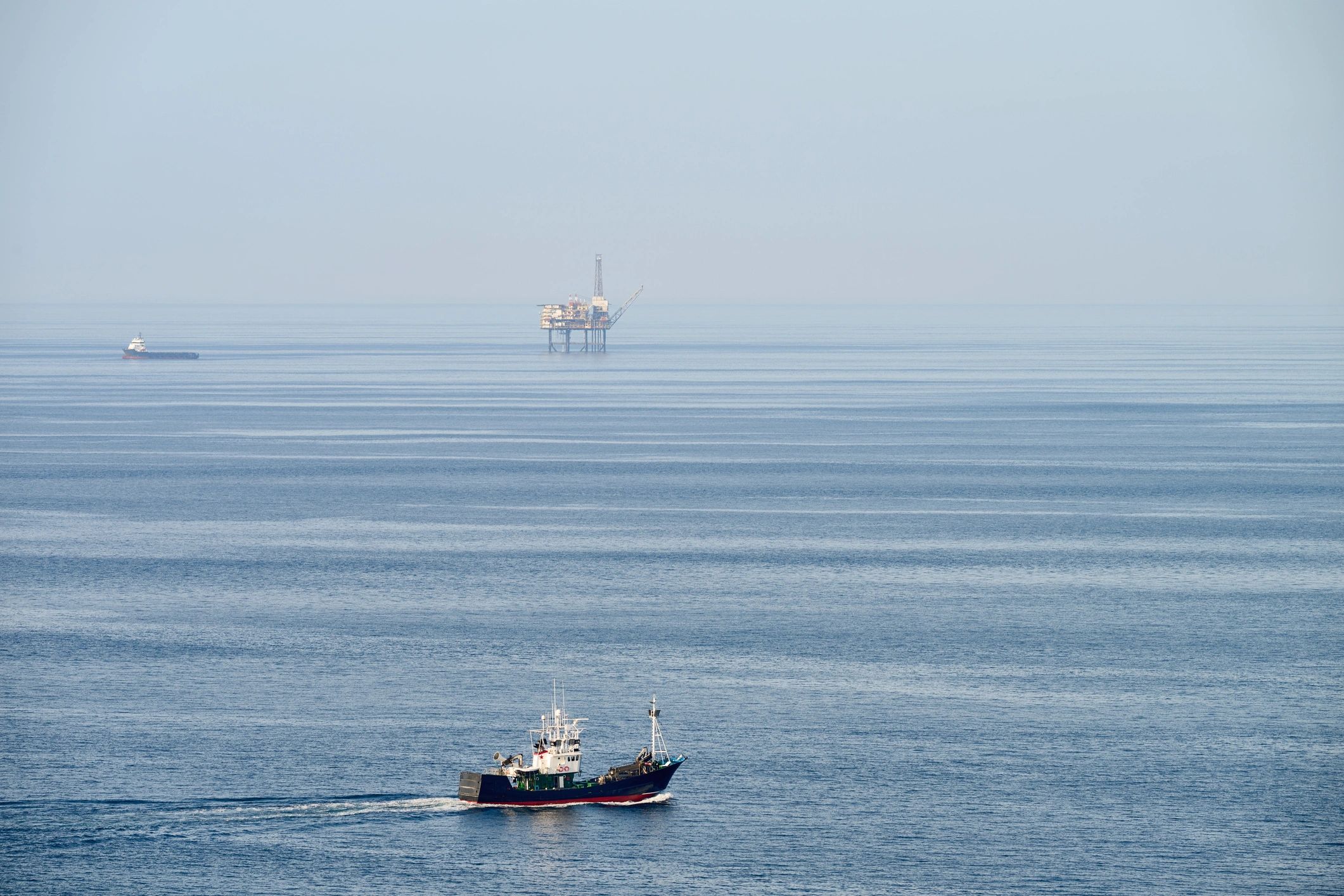 Fishing boat sailing past offshore oil rig in open sea